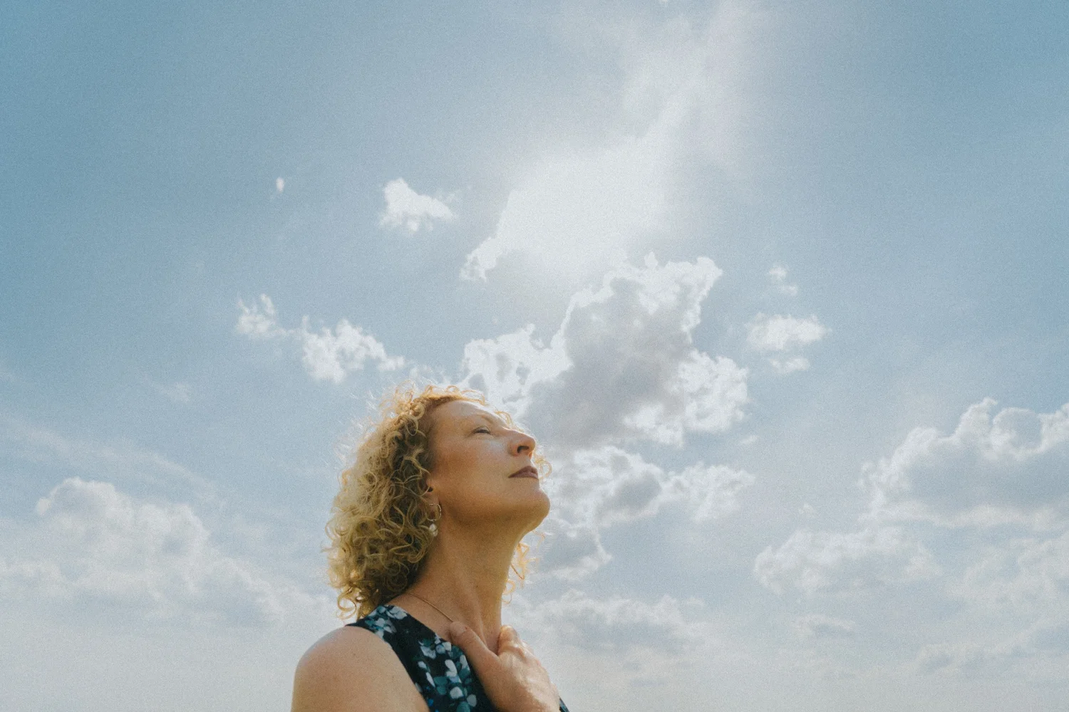 Portrait of a woman outdoors beneath a bright, cloud-filled sky.